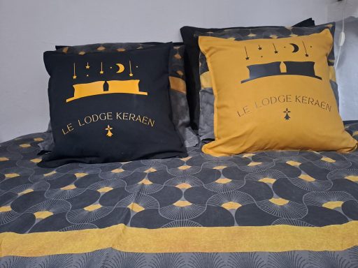 Deux coussins décoratifs sur un lit, un noir et un jaune, avec des motifs géométriques.