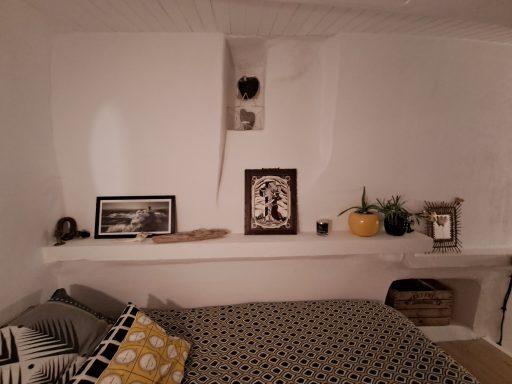 Chambre avec lit, étagère décorée, plante et photo en noir et blanc sur un mur blanc.