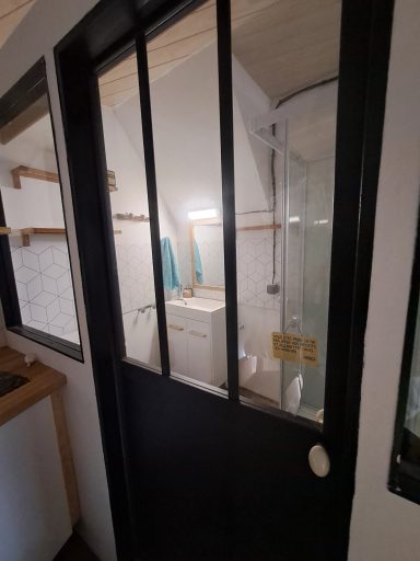 Salle de bain avec douche vitrée, lavabo, WC, machine à laver. Murs clairs.