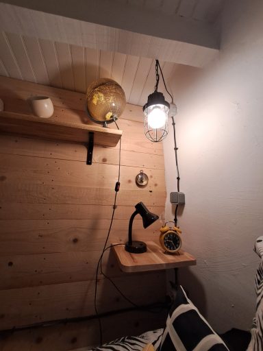 Coin de chambre avec étagère en bois, lampes suspendues et table en bois.