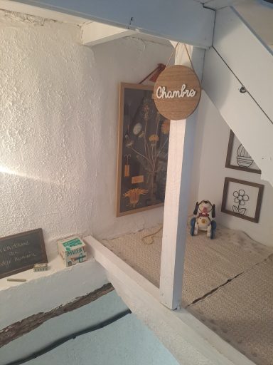 Espace intérieur avec des murs blancs, un panneau en bois et des œuvres accrochées.