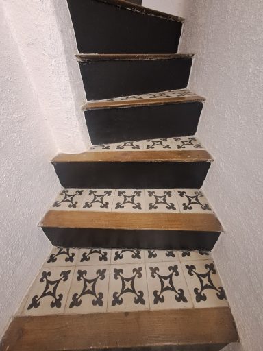 Escalier en bois avec marches noires et carrelage décoratif au sol.